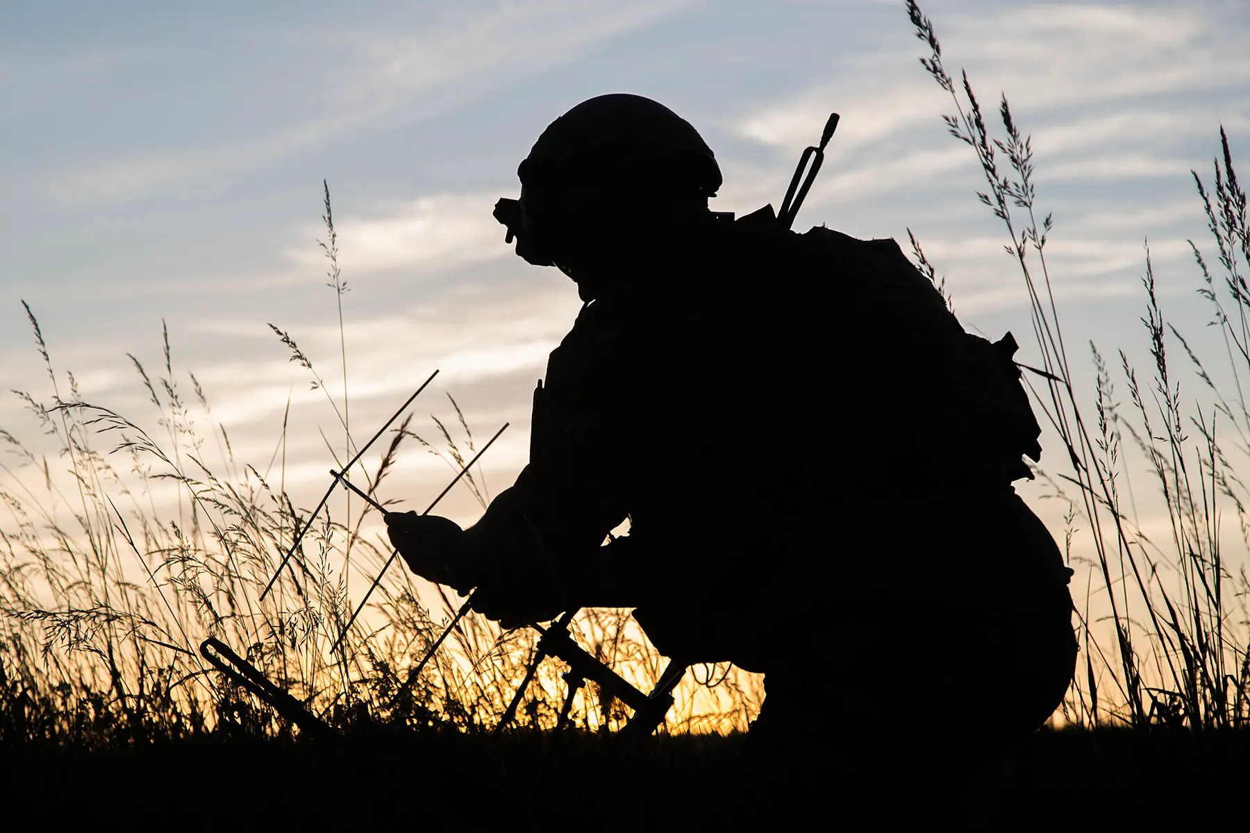 Silhouette of an operator setting up a satellite antenna in tall grass at sunset