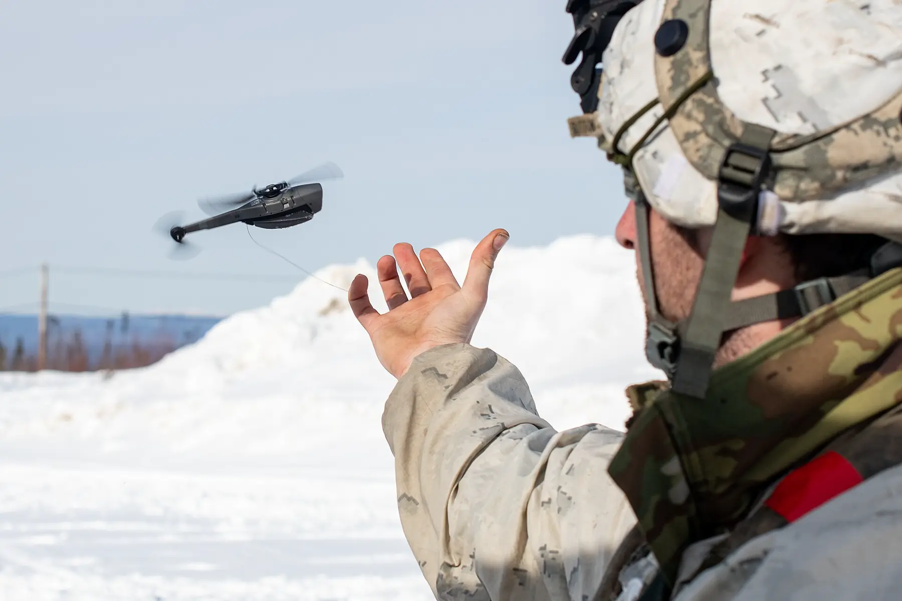 Operator releasing a palm-sized nano drone in a snowy landscape