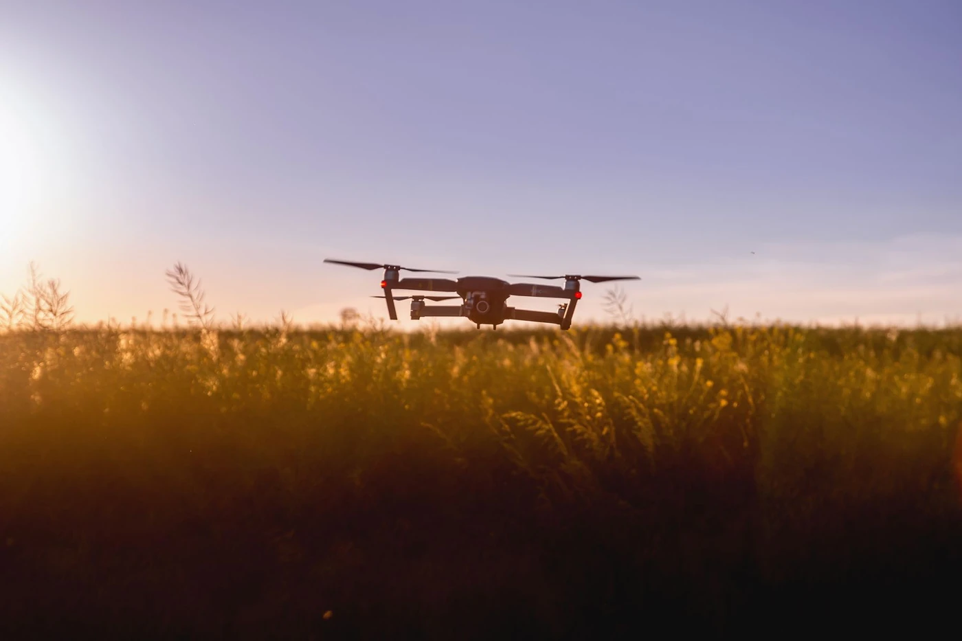 Quadcopter drone hovering over grassland at dusk
